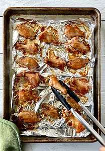 cooking tongs flipping baked chicken wings on a foil-lined baking sheet