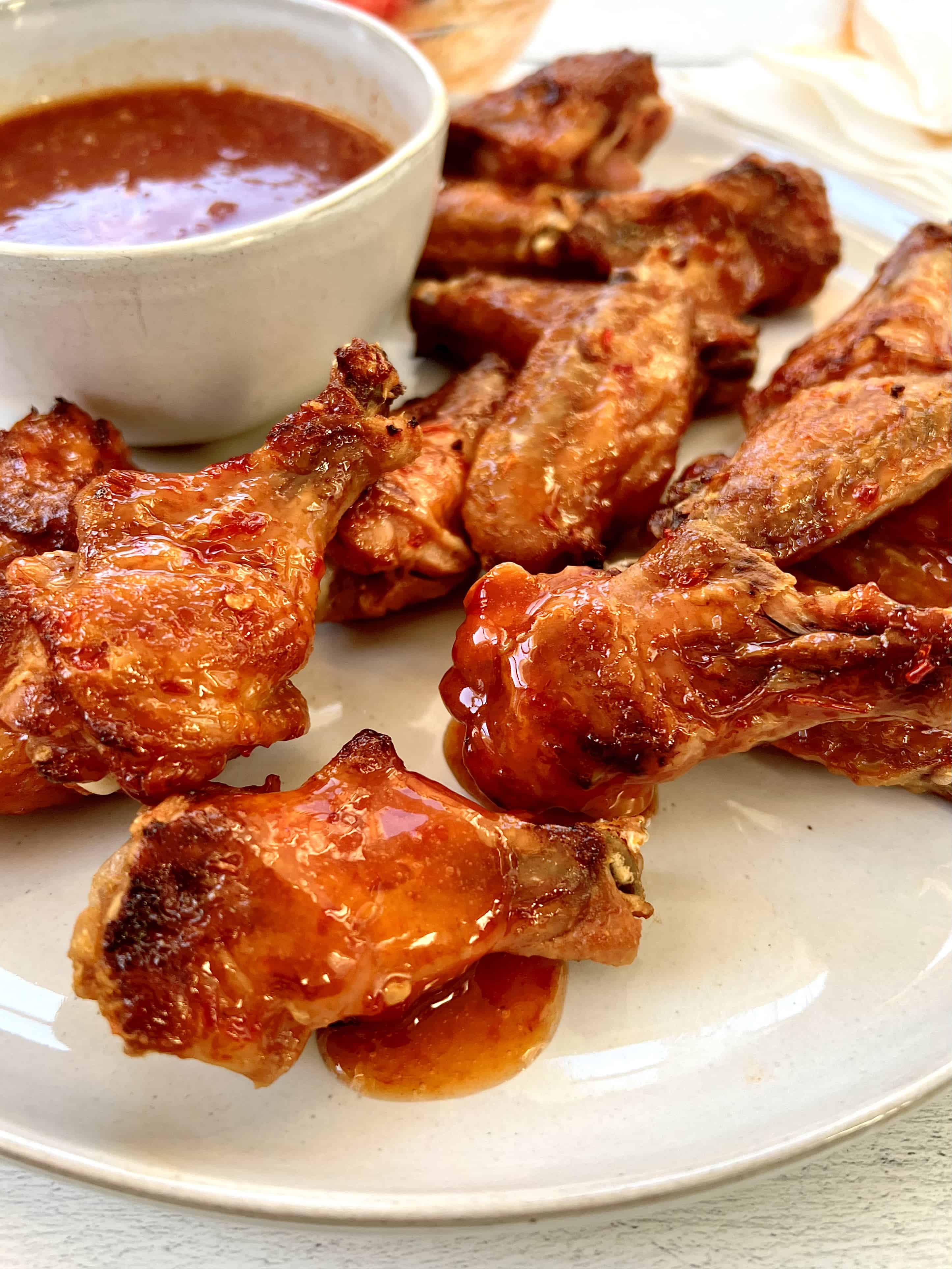 baked paleo wings on a platter with a small bowl of spicy honey sauce