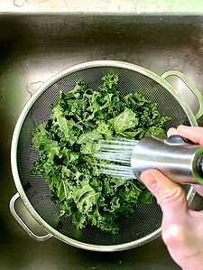 rinsing kale leaves in a colander in a sink