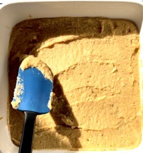 smoothing the plantain bread batter with a blue spatula in a white square baking dish