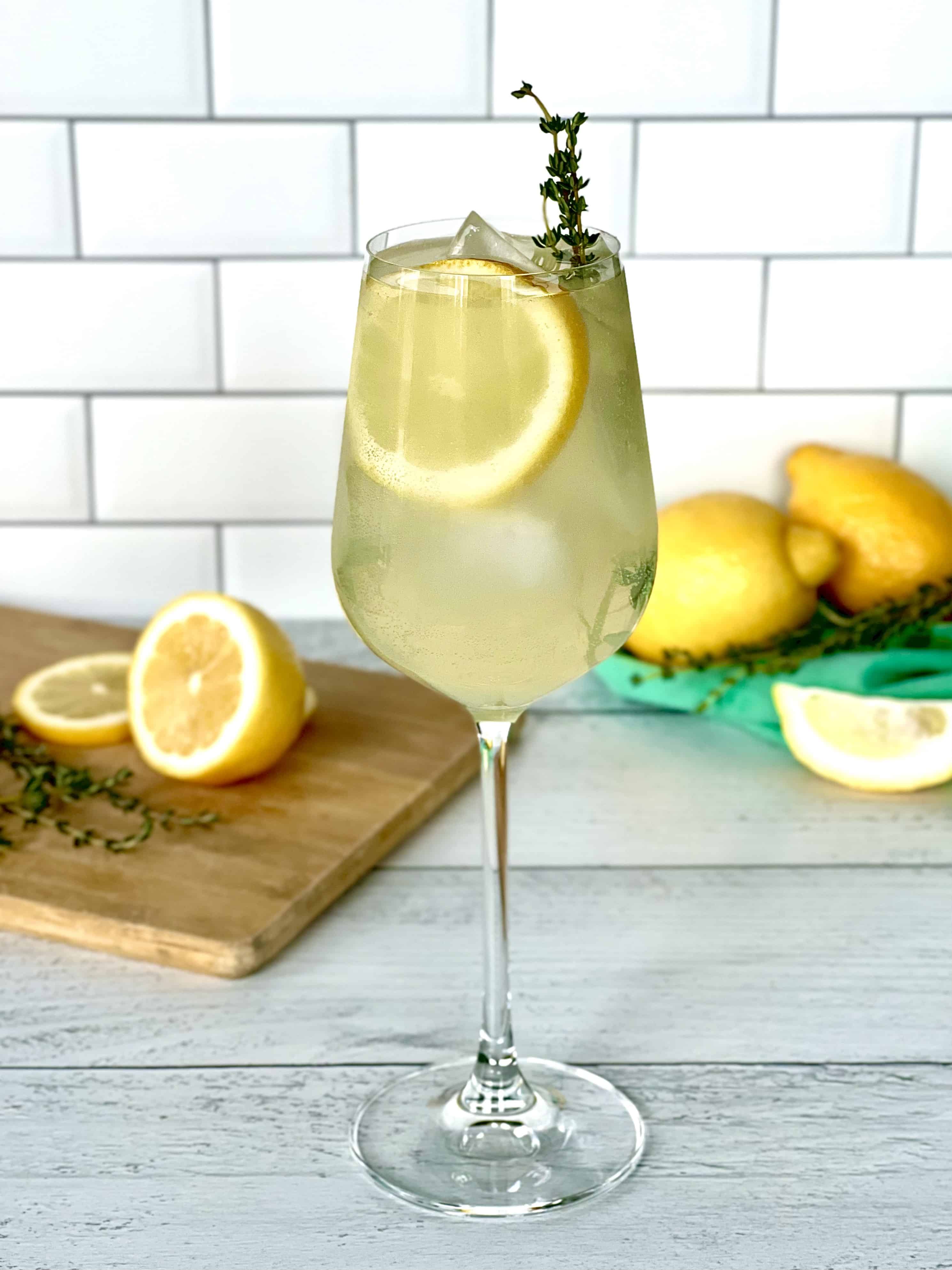 Limoncello spritzer with prosecco in a wine glass with ice, a lemon slice and sprig of thyme.