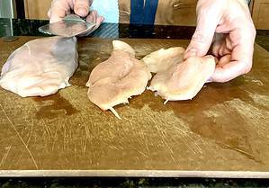Cutting chicken breasts into cutlets on a cutting board.