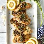 Whole30 chicken piccata on a long white platter with lemon slices.