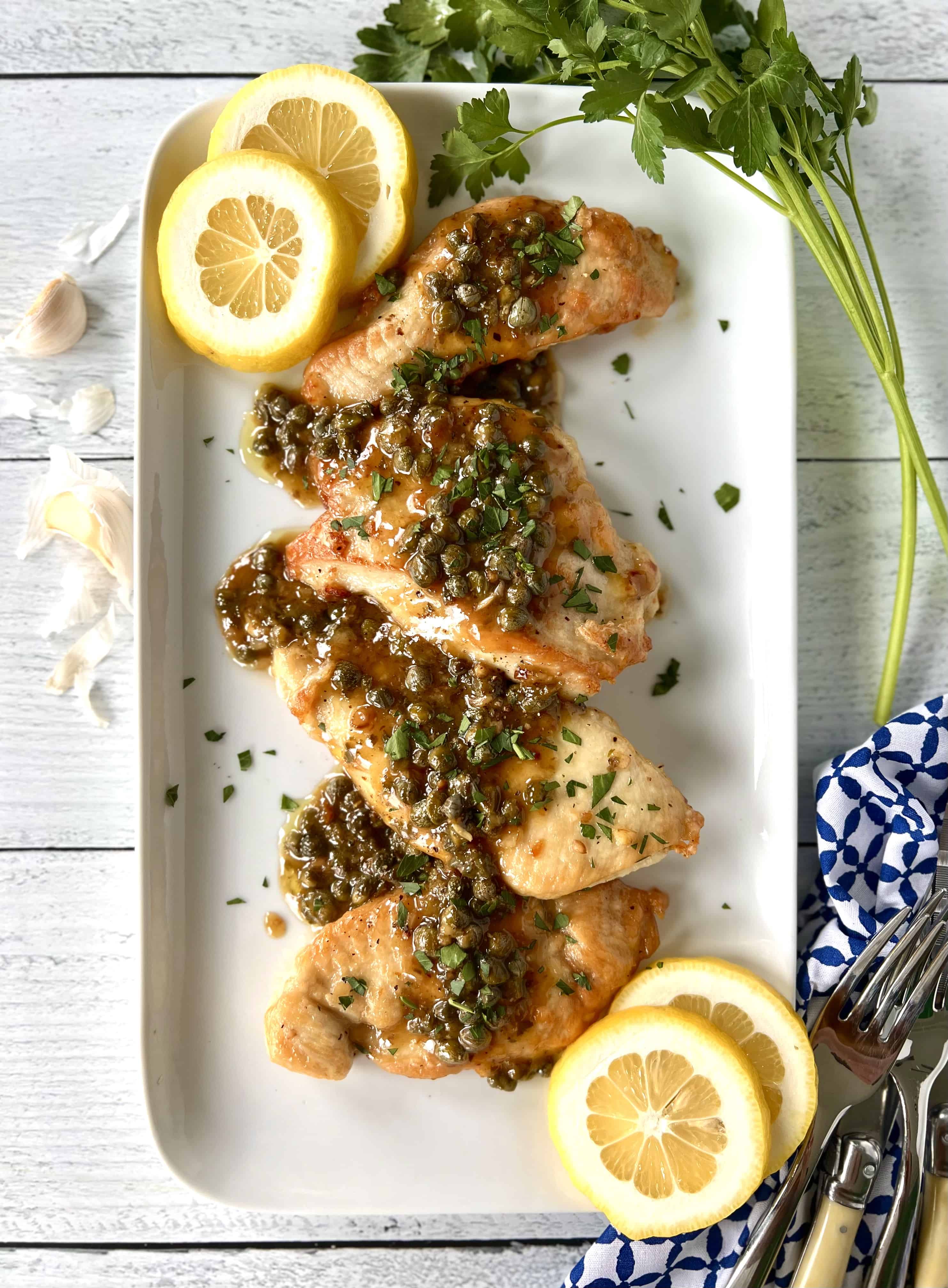 Whole30 chicken piccata on a long white platter with lemon slices.