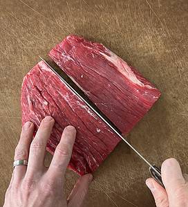 Cutting flank steak in half on a cutting board.