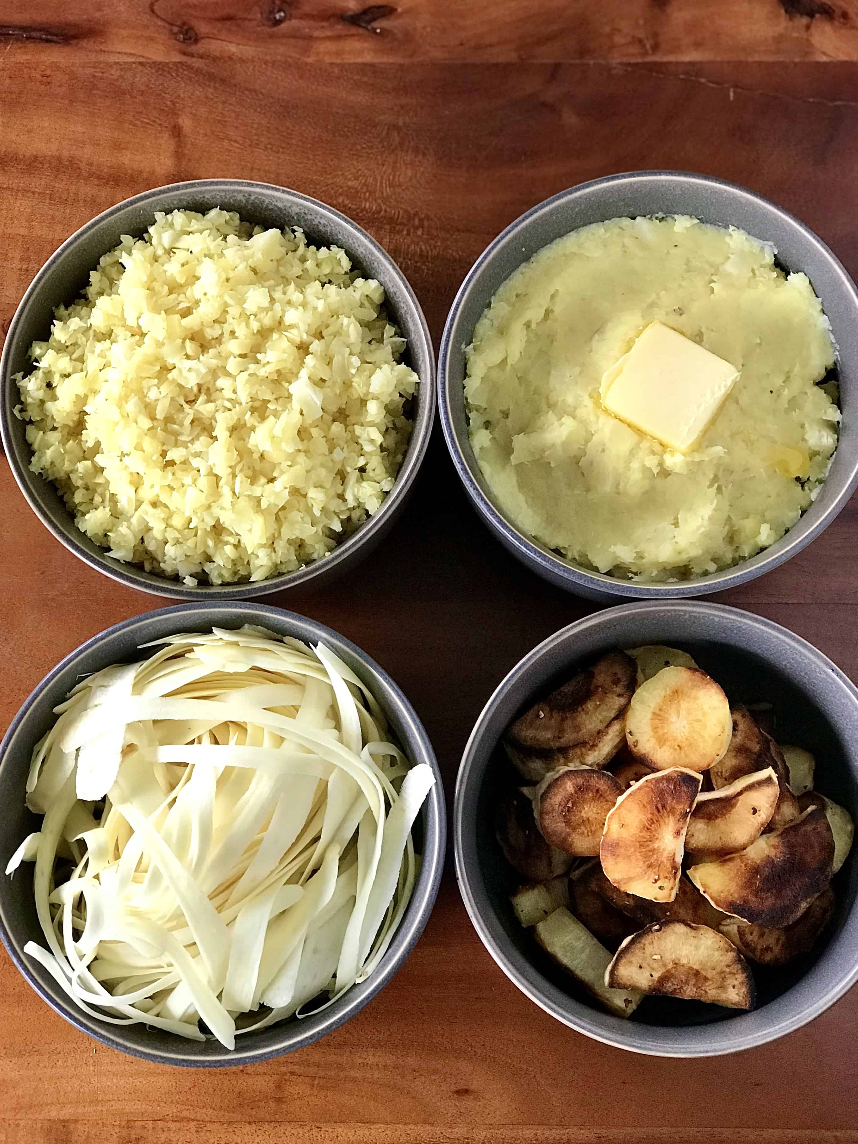 Bowls of roasted parsnips, mashed parsnips, parsnip noodles and parsnip rice on a wooden table.