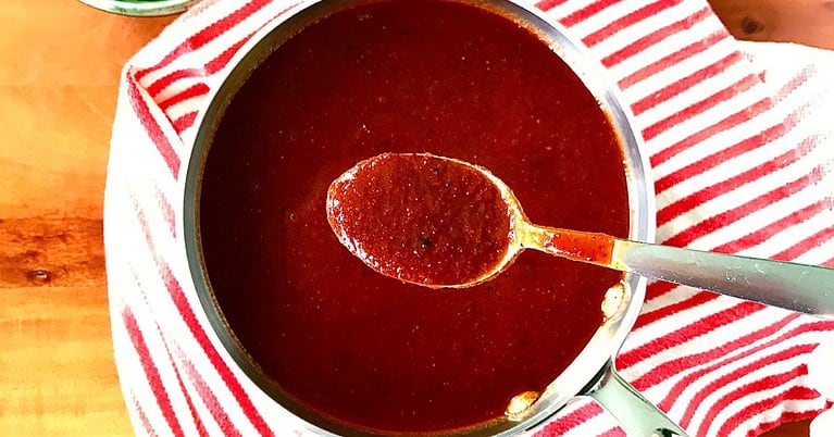 Healthy BBQ Sauce in a small pan on top of a red and white striped towel with a spoon over the pan holding some sauce.