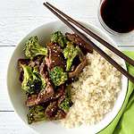 Paleo beef stir fry in a white bowl with cauliflower rice and chopsticks, next to a green napkin.
