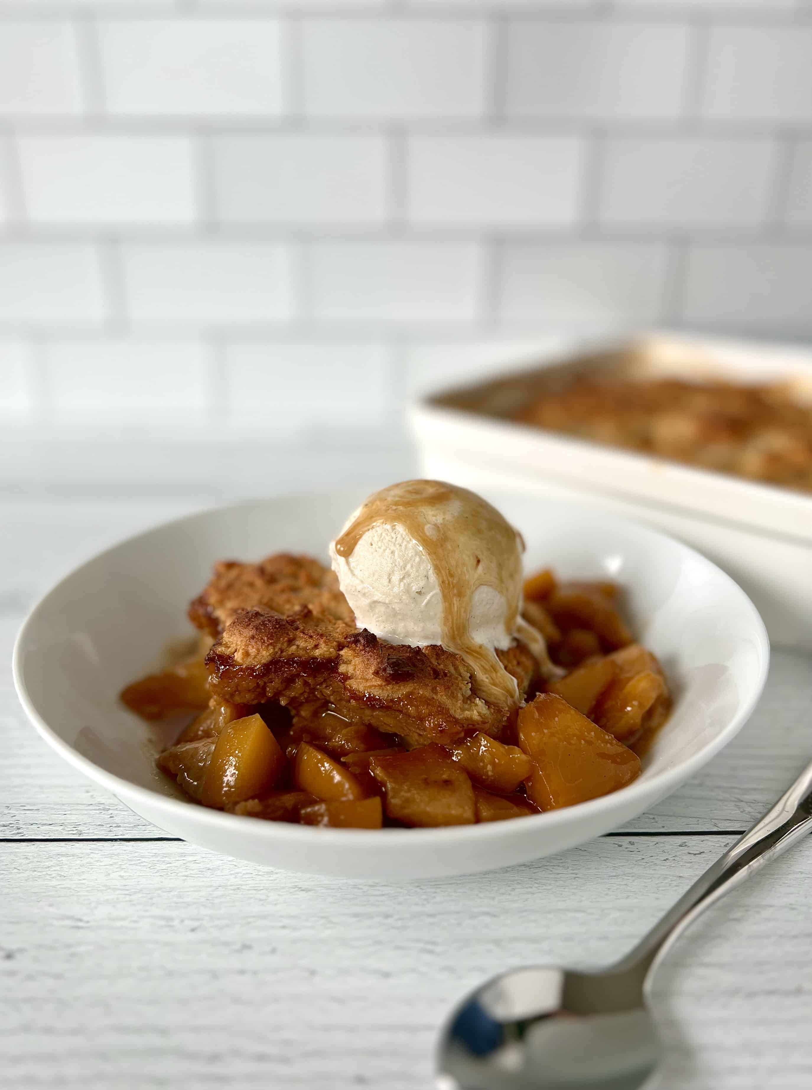 Paleo cobbler in a white bowl with ice cream on top and sauce drizzled over the ice cream.
