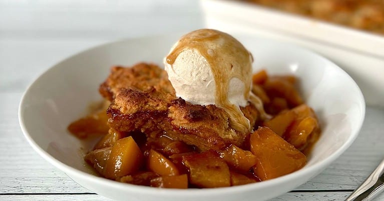 Gluten-free peach cobbler in a white bowl topped with ice cream.
