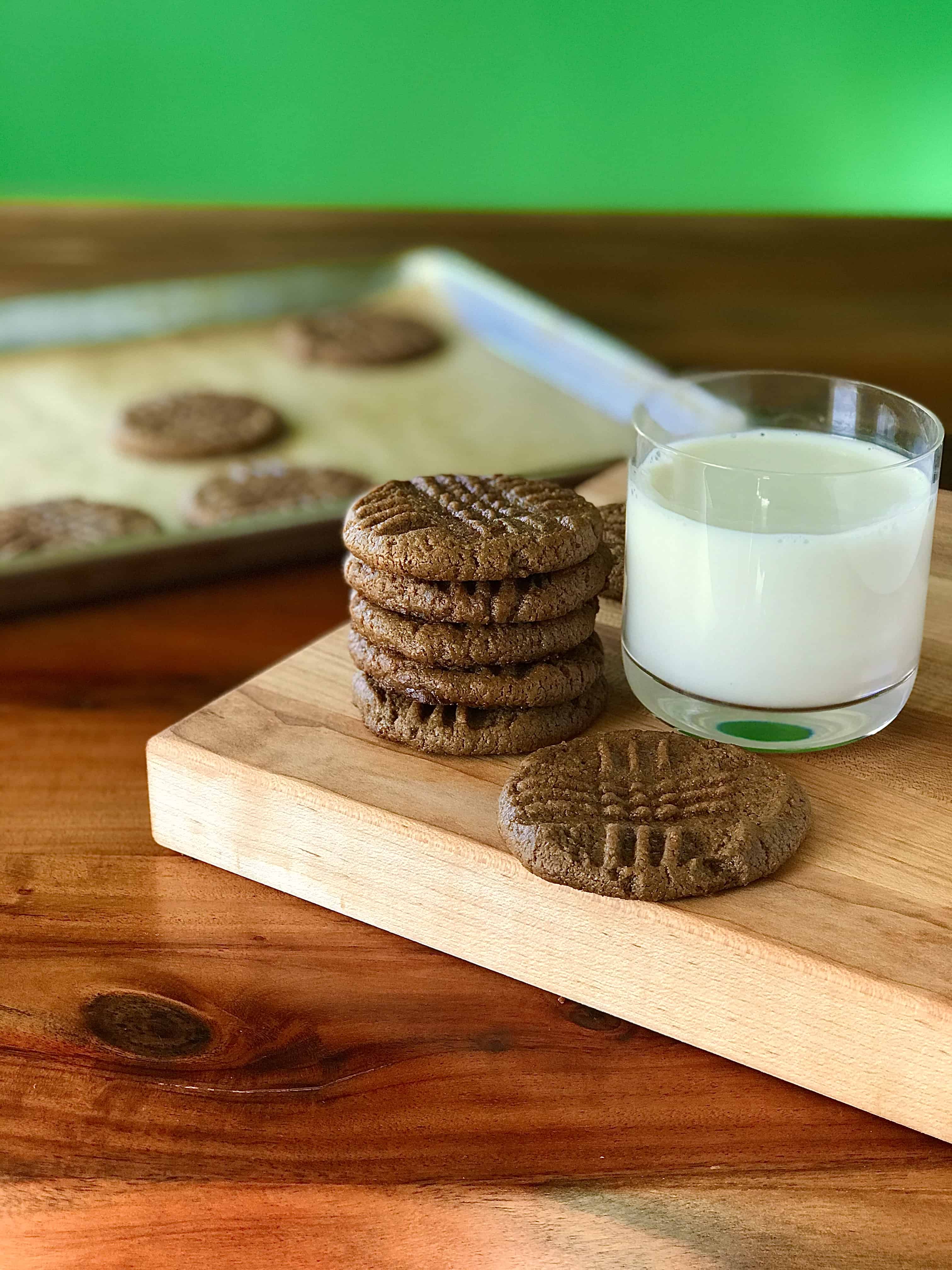 Flourless peanut butter cookies on a wooden cutting board with a glass of milk.