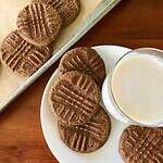 Gluten-free peanut butter cookies on a plate with a glass of milk and on a parchment-lined baking sheet.