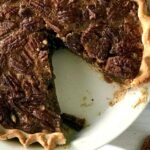 Healthier pecan pie in a pie dish with a slice missing.