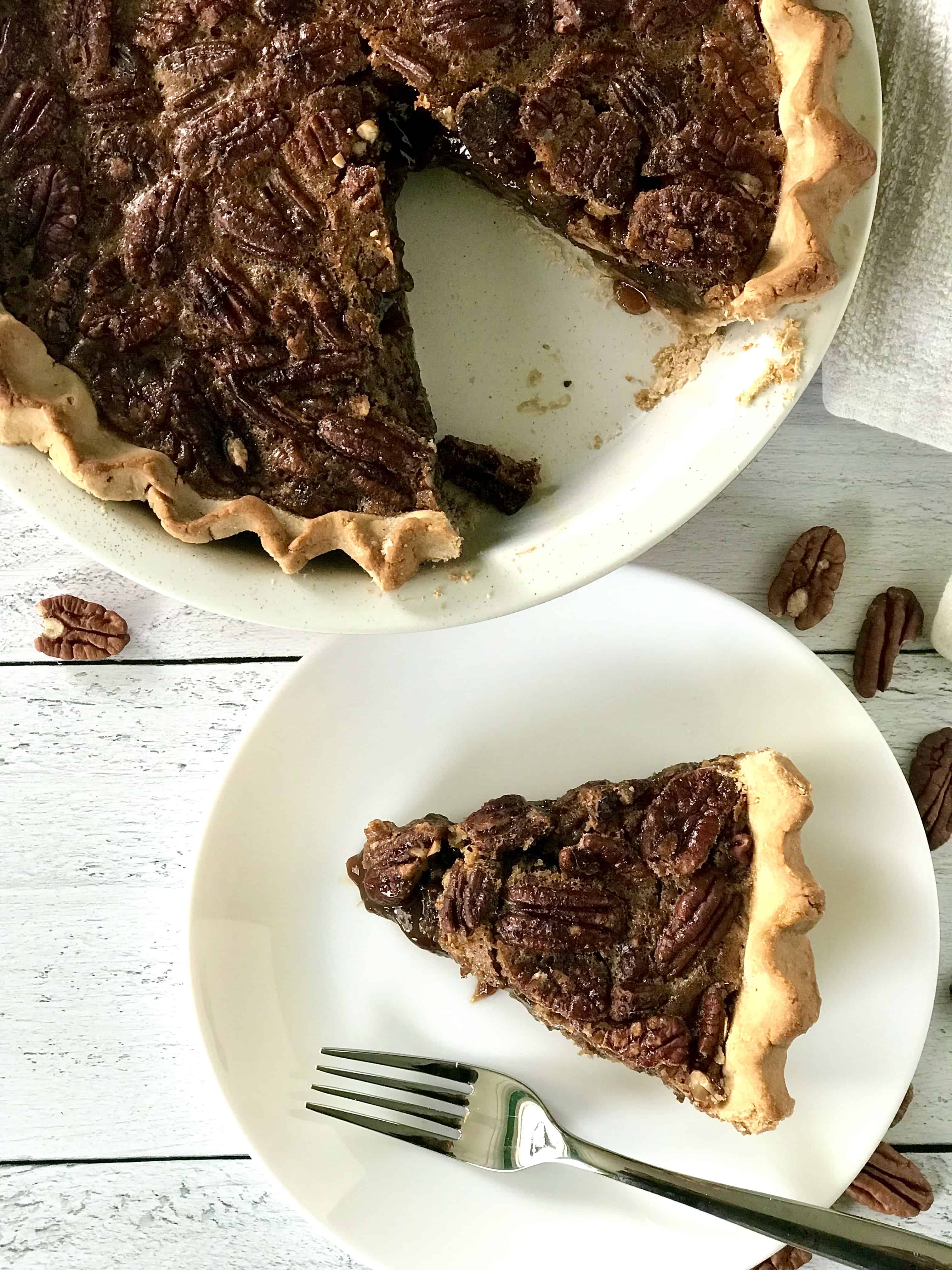 Gluten-free pecan pie in a pie dish with a slice missing and the slice on a white plate with a fork.