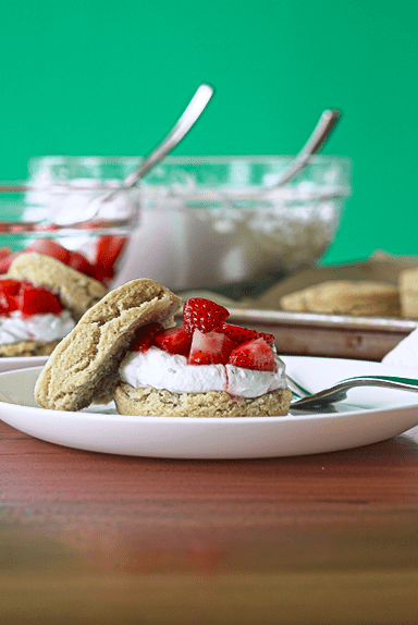 Strawberries and whipped coconut cream on grain-free biscuits on white plates with forks.
