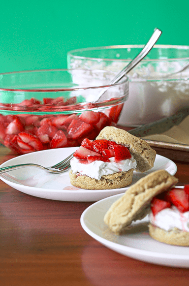 Paleo biscuits topped with strawberries and whipped coconut cream on white plates.