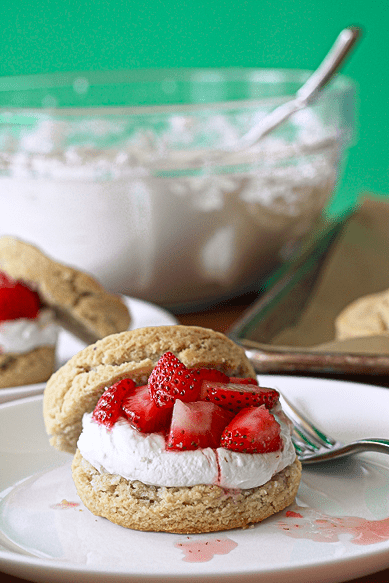 Almond flour biscuits topped with whipped coconut cream and strawberries on white plates with forks.