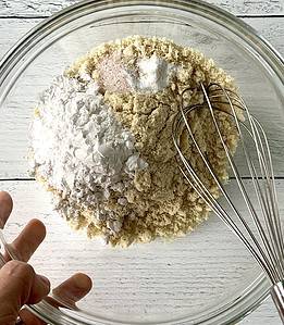 A hand holding a glass bowl with the dry ingredients for a cobbler topping and a whisk.