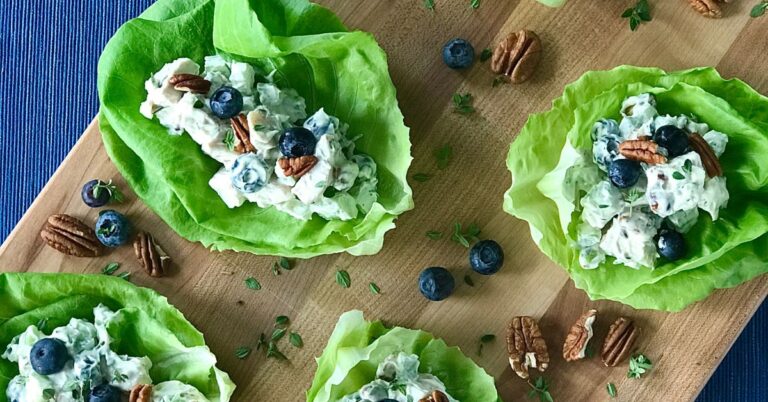 Whole 30 chicken salad with blueberries and pecans in lettuce cups on a wooden cutting board.