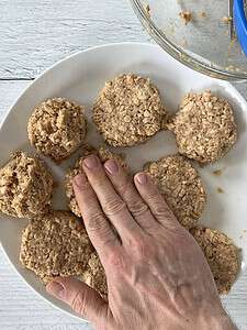 Flattening salmon cakes on a white plate.