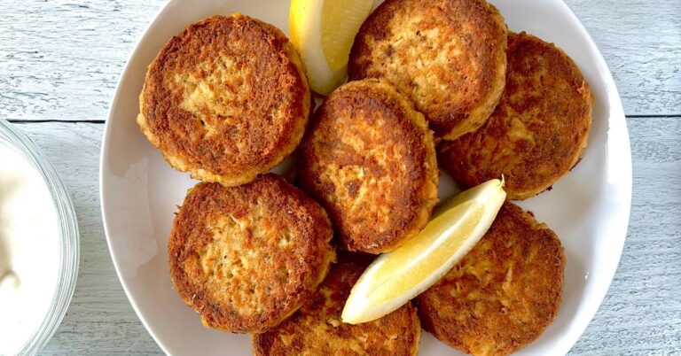 Paleo Salmon Cakes piled on a white plate with lemon wedges.