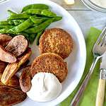 Paleo salmon cakes on a white plate with a dollop of aioli, roasted potatoes and sugar snap peas.