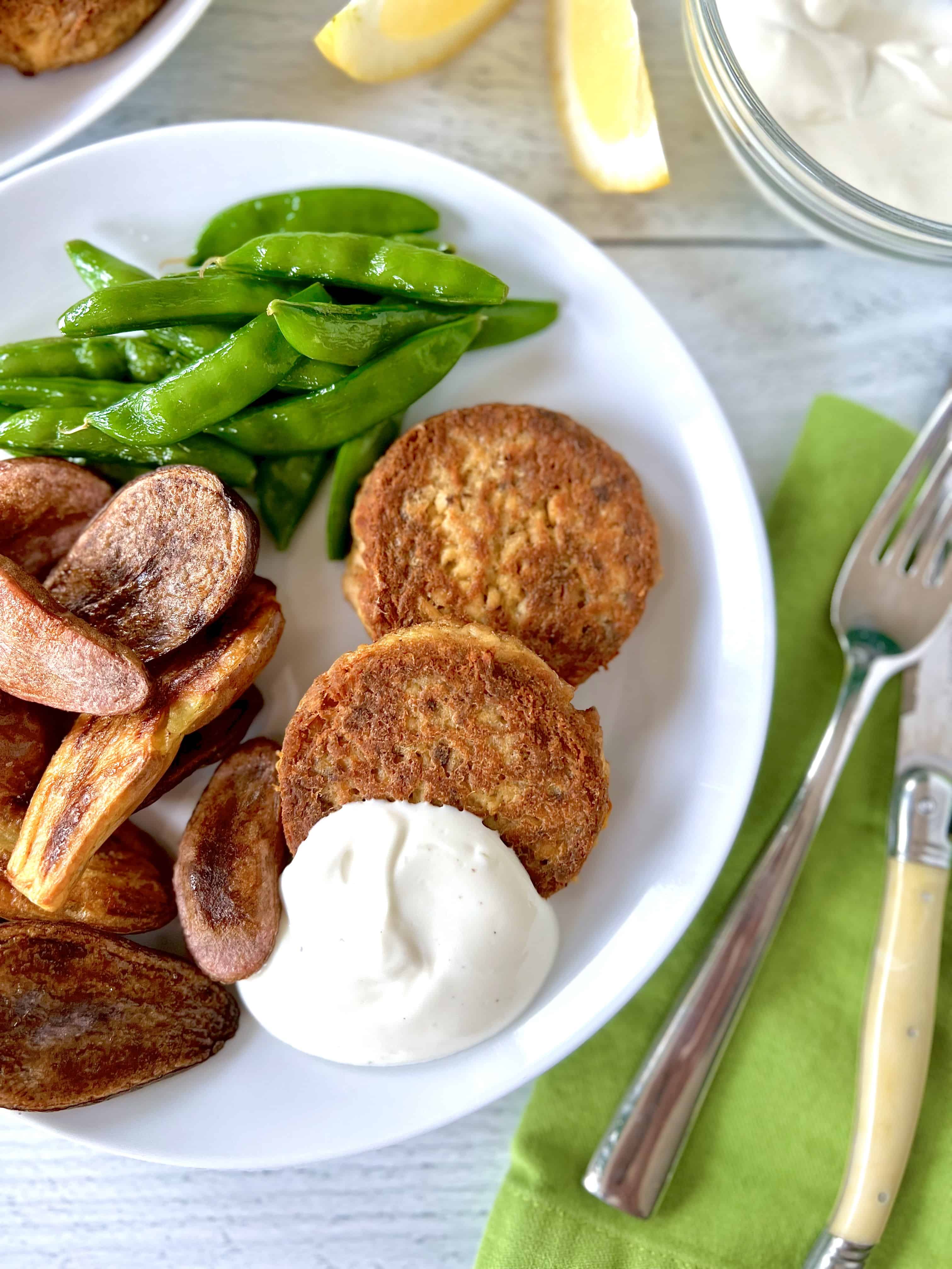 Paleo salmon cakes on a white plate with a dollop of aioli, roasted potatoes and sugar snap peas.