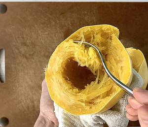 Scooping noodles out of a spaghetti squash with a fork.