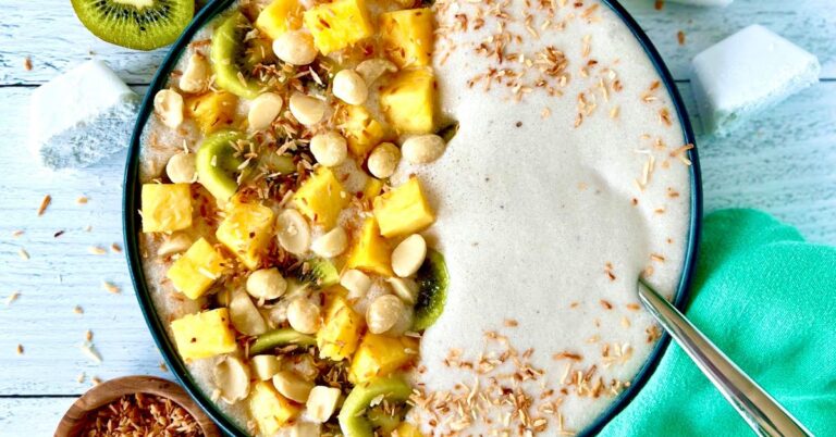 Coconut banana smoothie bowl topped with pineapple, kiwi, macadamias and toasted shredded coconut.
