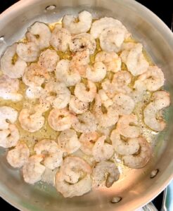 Raw shrimp in a large stainless steel pan with ghee and olive oil.