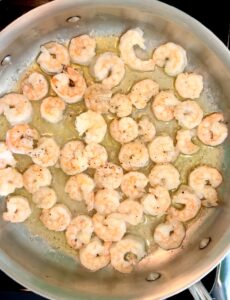 Shrimp cooking in a large stainless steel pan with ghee and olive oil.
