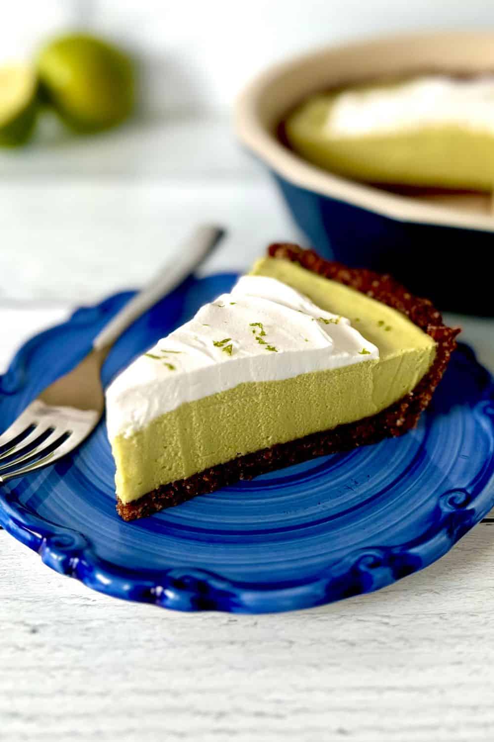 A slice of avocado key lime pie on a blue-swirled plate with a fork.