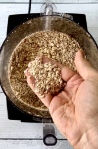 A hand holding up some ground almonds over a food processor.