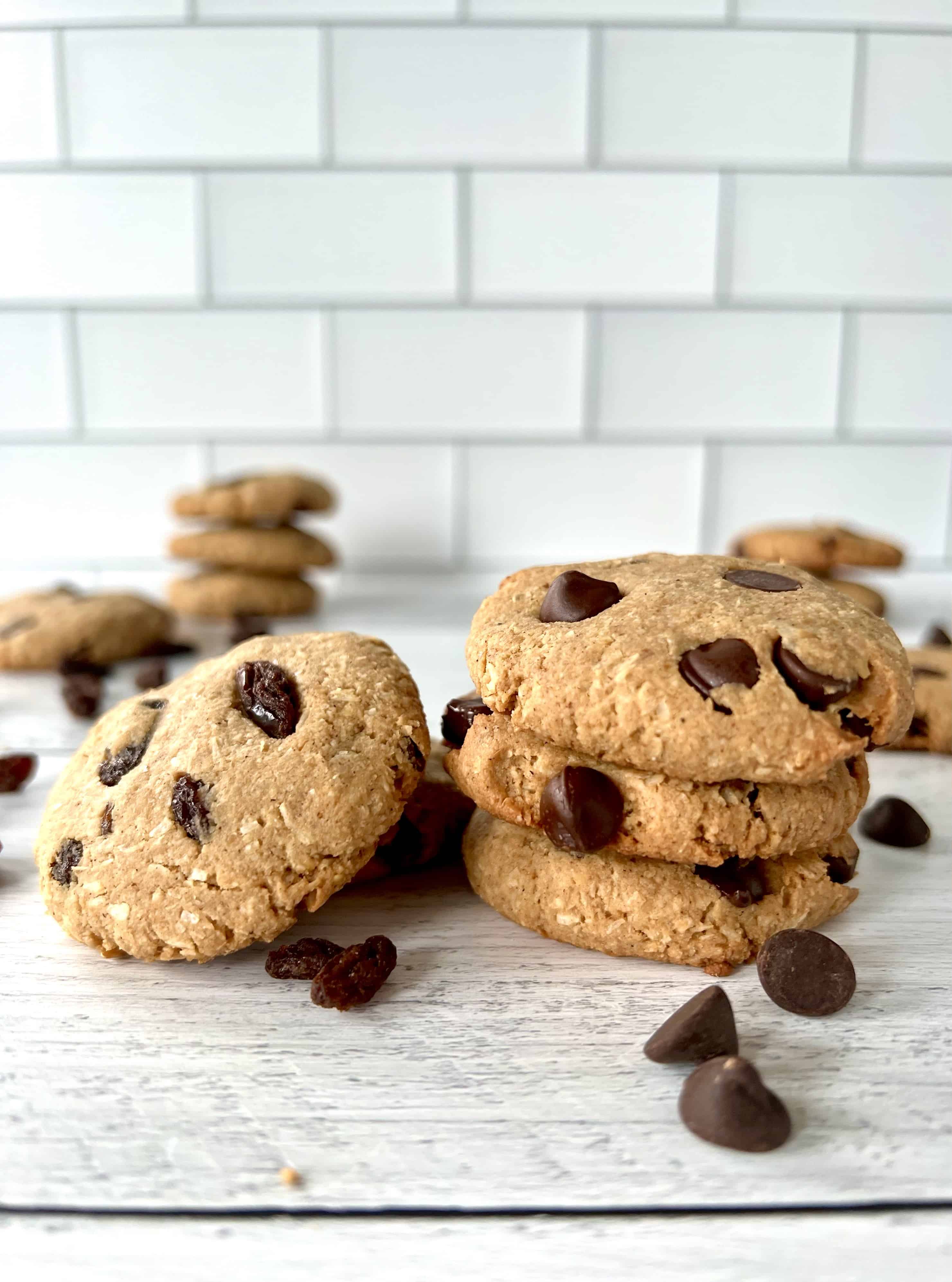 Gluten-free oatmeal cookies with raisins or chocolate chips stacked on a white wooden table.