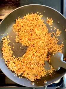 Stirring seasoned cauliflower rice in a nonstick pan.
