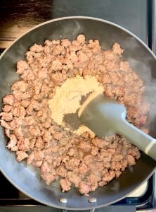 Stirring spices into ground beef in a nonstick pan.