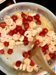 Stirring cherry tomatoes and shrimp in ghee and olive oil in a large stainless steel pan.