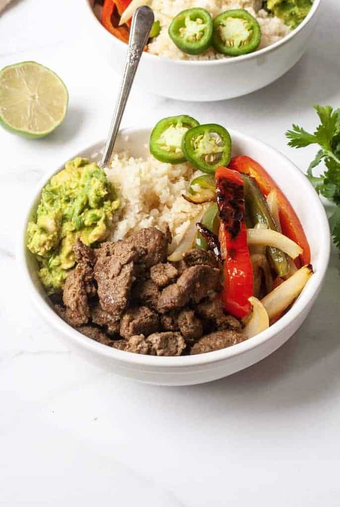 Beef burrito bowls in a white bowl on a white table.