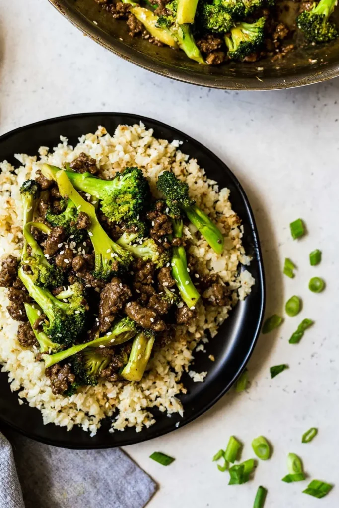 Grond beef and broccoli on top of cauliflower rice on a black plate.