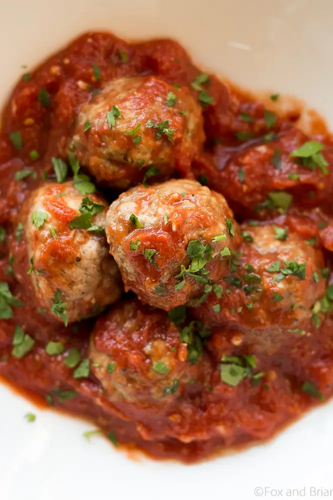 Meatballs in tomato sauce, sprinkled with basil, in a white bowl.