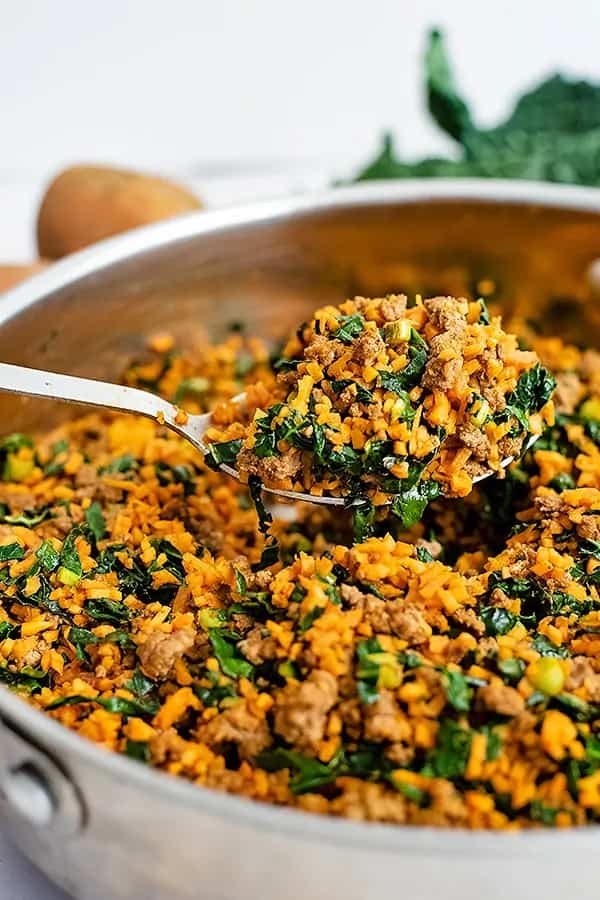Sweet potato rice breakfast skillet in a metal pan, with some getting scooped up by a metal serving spoon.