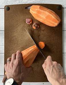 Chopping the ends off sweet potatoes on a cutting board.