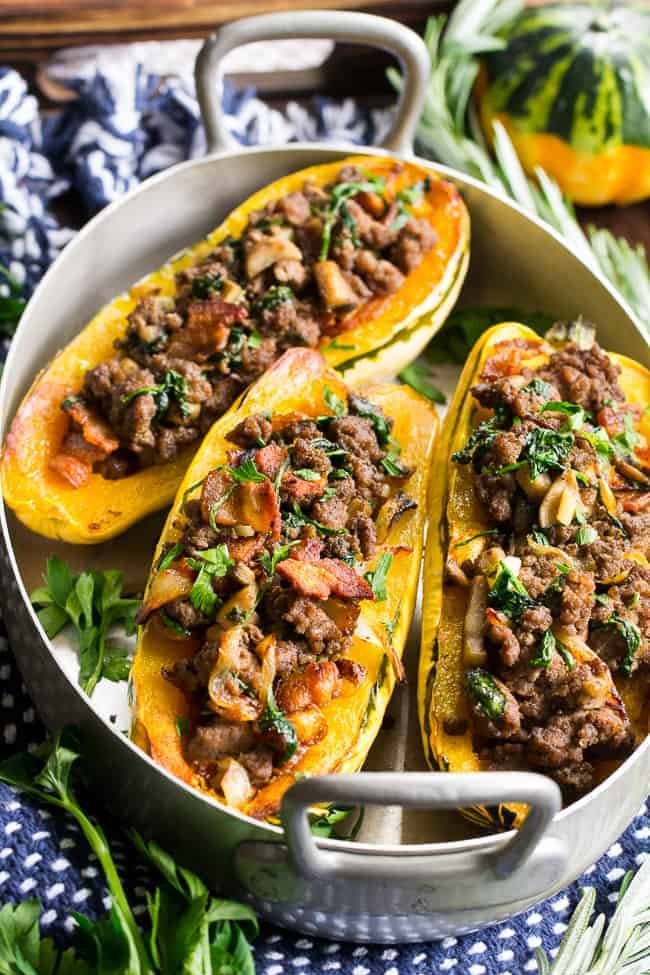 Delicata squash stuffed with beef, bacon and vegetables in a large metal pan.