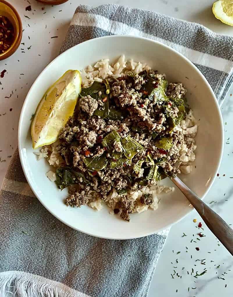 Ground beef and chopped grape leaves with a lemon wedge in a shallow white bowl.