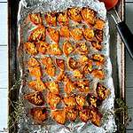 Slightly charred slices of sweet potato on a foil-lined baking sheet with a spatula and thyme sprigs.