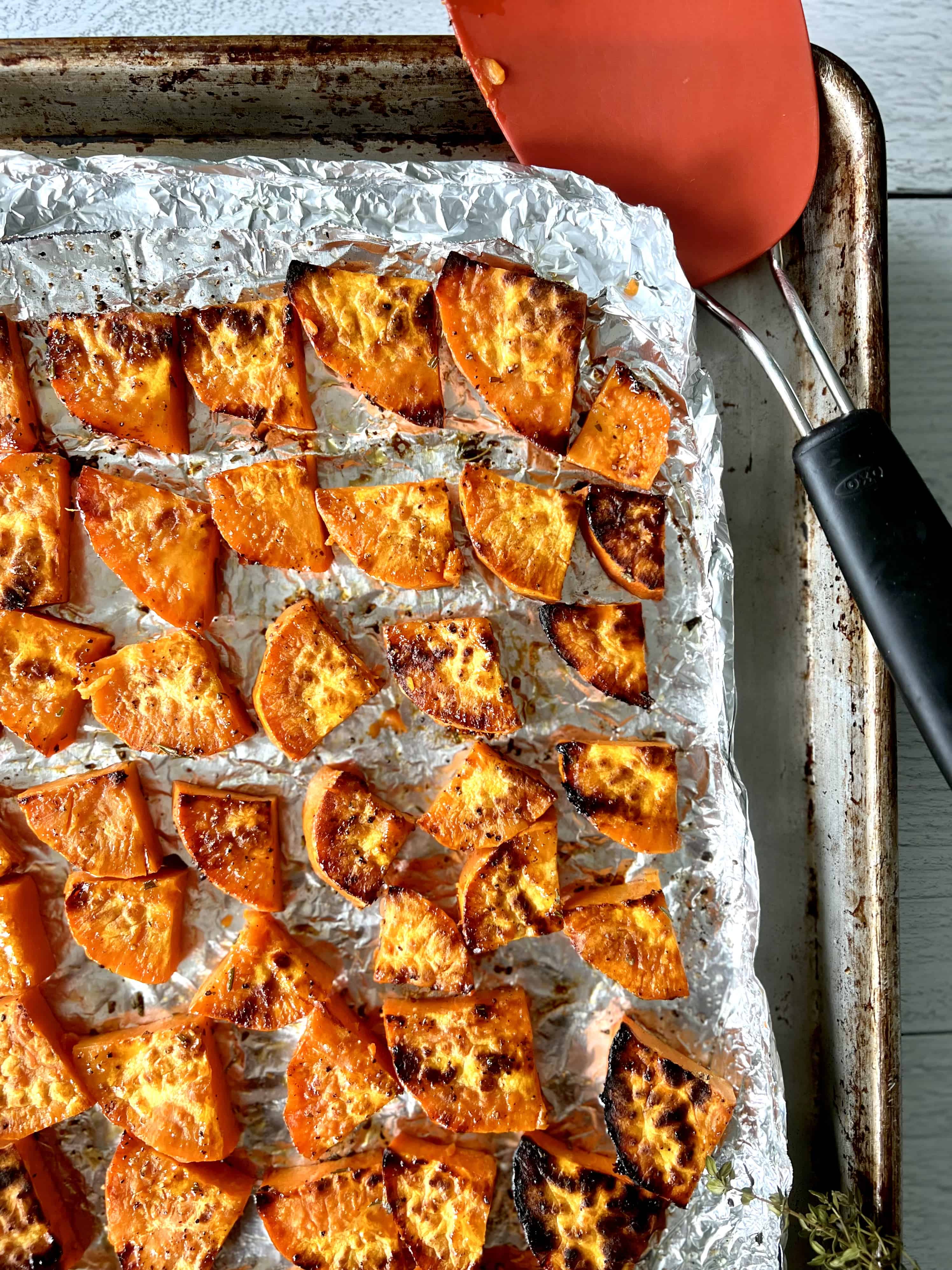 A foil-lined baking sheet with slices of grilled yams on it, and a spatula.
