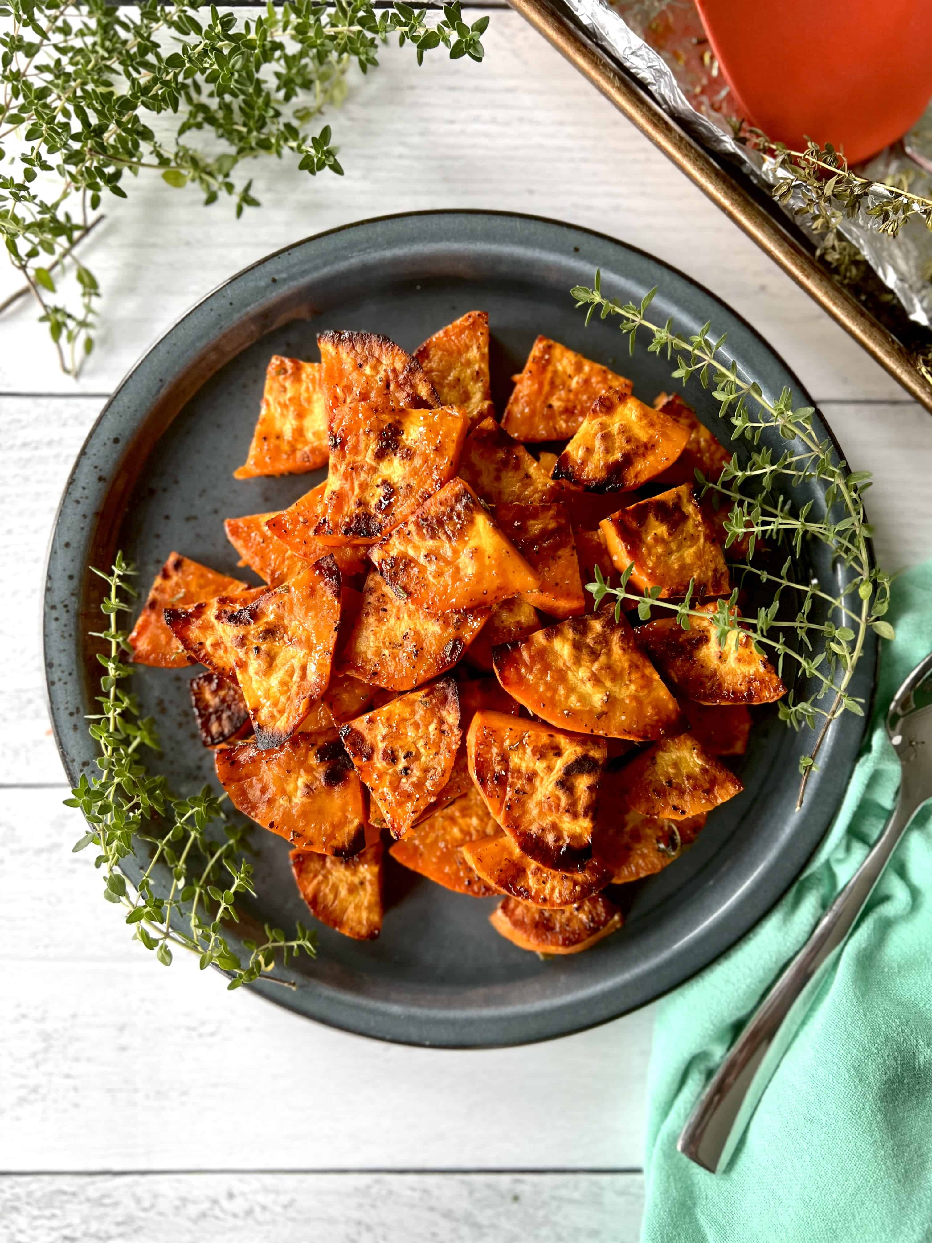 Slices of caramelized sweet potatoes piled on a blue plate with thyme sprigs.