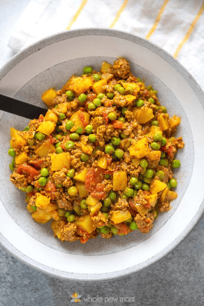 Ground beef curry with potatoes and peas in a white and gray bowl.