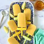 Mango, yogurt, honey and lime popsicles on a blue and white patterned platter with lime wedges.