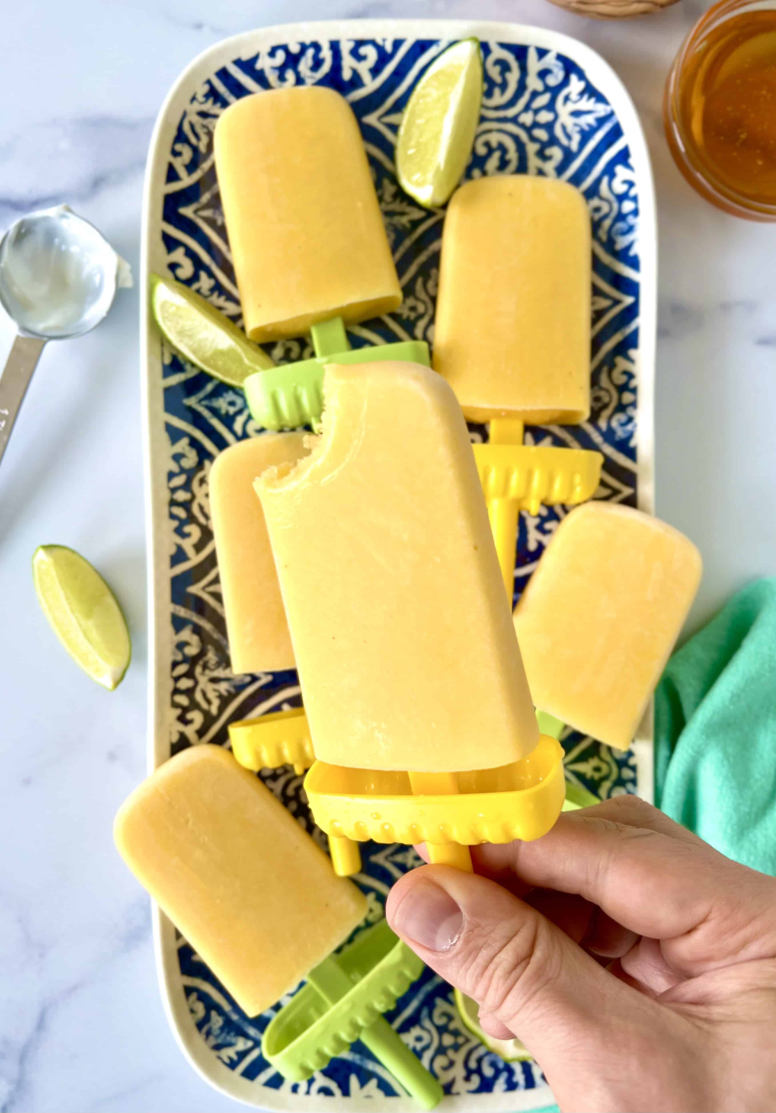 Frozen mango and yogurt popsicles on blue and white patterned platter with a hand holding one of the pops above them.